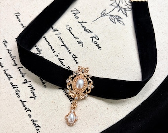 May include: A black velvet choker necklace featuring a gold-toned filigree pendant centered with an oval faux pearl and small clear crystals. A smaller teardrop-shaped faux pearl hangs from the bottom of the pendant, and the necklace includes a gold-toned metal chain extender.
