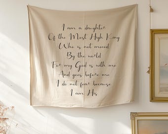 Op de afbeelding: Beige wandkleed met zwarte tekst. De tekst luidt: "Ik ben een dochter van de Allerhoogste Koning die niet bewogen wordt door de wereld, want mijn God is met mij en gaat mij voor, ik vrees niet want ik ben van Hem."