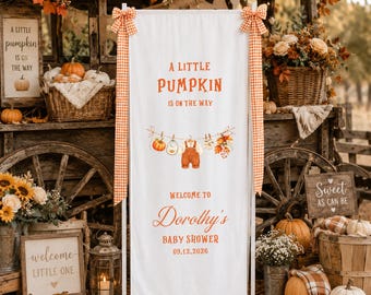 May include: A white vertical fabric banner featuring orange text that reads A LITTLE PUMPKIN IS ON THE WAY, WELCOME TO Dorothy's BABY SHOWER, and 09.12.2026. The banner displays a graphic of baby clothes on a clothesline and orange gingham bows.