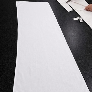 Puede incluir: Una gran tela blanca de poli&eacute;ster colocada sobre una superficie negra. La palabra "POLYESTER" est&aacute; impresa en blanco en la esquina superior izquierda. Una persona est&aacute; cortando tela con tijeras en el fondo.