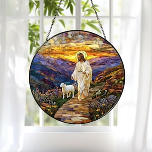 Op de afbeelding: Rond gebrandschilderd glazen raam met een religieuze scène. Het kunstwerk toont een figuur in witte gewaden met een halo, lopend met een lam op een stenen pad. De achtergrond toont een zonsondergang boven bergen.