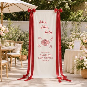 May include: A tall, rectangular white fabric banner featuring red text and graphics. The text reads "Slice, Slice, Baby" and "WELCOME TO ANGELA'S BABY SHOWER 09.22.2026". Red ribbon bows are attached to the top corners with long ribbons hanging down.