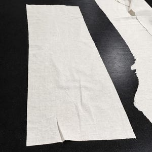 Puede incluir: Primer plano de piezas de tela de algod&oacute;n y lino blanco sobre una superficie negra. El texto "COTTON LINEN" se muestra en blanco. La tela est&aacute; cortada en varias formas, lo que sugiere un proyecto de costura o manualidades.