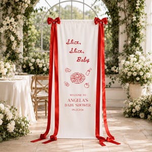 May include: A white vertical fabric banner featuring red text that reads "Slice, Slice, Baby" and "WELCOME TO ANGELA'S BABY SHOWER 09.22.2026". The banner includes red line art of a pizza, a baby bottle, a pacifier, and a tomato, accented by red ribbons.