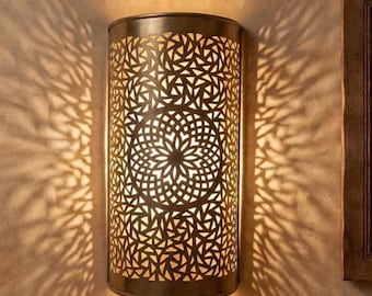 May include: A semi-cylindrical wall sconce featuring a metallic finish with an intricate, laser-cut geometric pattern. The light fixture emits a warm glow, casting complex, symmetrical shadow patterns onto the surrounding wall surface.