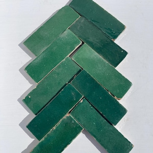 Può includere: Una collezione di piastrelle rettangolari verde smeraldo disposte a spina di pesce. Le piastrelle hanno una finitura lucida e sono presentate su una superficie bianca. Ideali per progetti di interior design e decorazione.