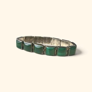 Könnte beinhalten: Ein Gliederarmband mit rechteckigen, silberfarbenen Metallsegmenten, die sich mit glatten, dunkelgrünen Steineinlagen abwechseln. Das Armband ist mit einer Reihe von Scharnierverbindungen konstruiert, was ein flexibles Band mit polierter Oberfläche ergibt.