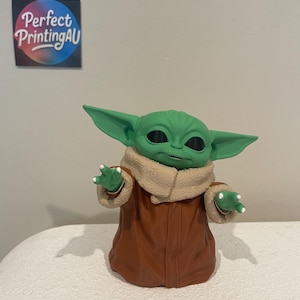 May include: A green figurine of a character with large ears, wearing a brown coat with a tan collar. The figurine has black eyes and small white claws. The text "Perfect PrintingAU" is on a sticker in the background.