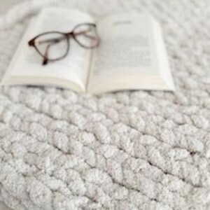 Hand-knit French Vanilla blanket with book and reading glasses styled on top, cozy and relaxing home decor scene.