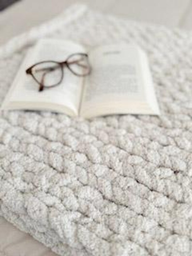 Hand-knit French Vanilla blanket with book and reading glasses styled on top, cozy and relaxing home decor scene.