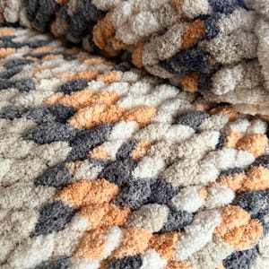 Close-up of chunky hand-knit blanket in Toasted Birch multi-tone yarn, showing plush stitches in cream, tan, and gray.