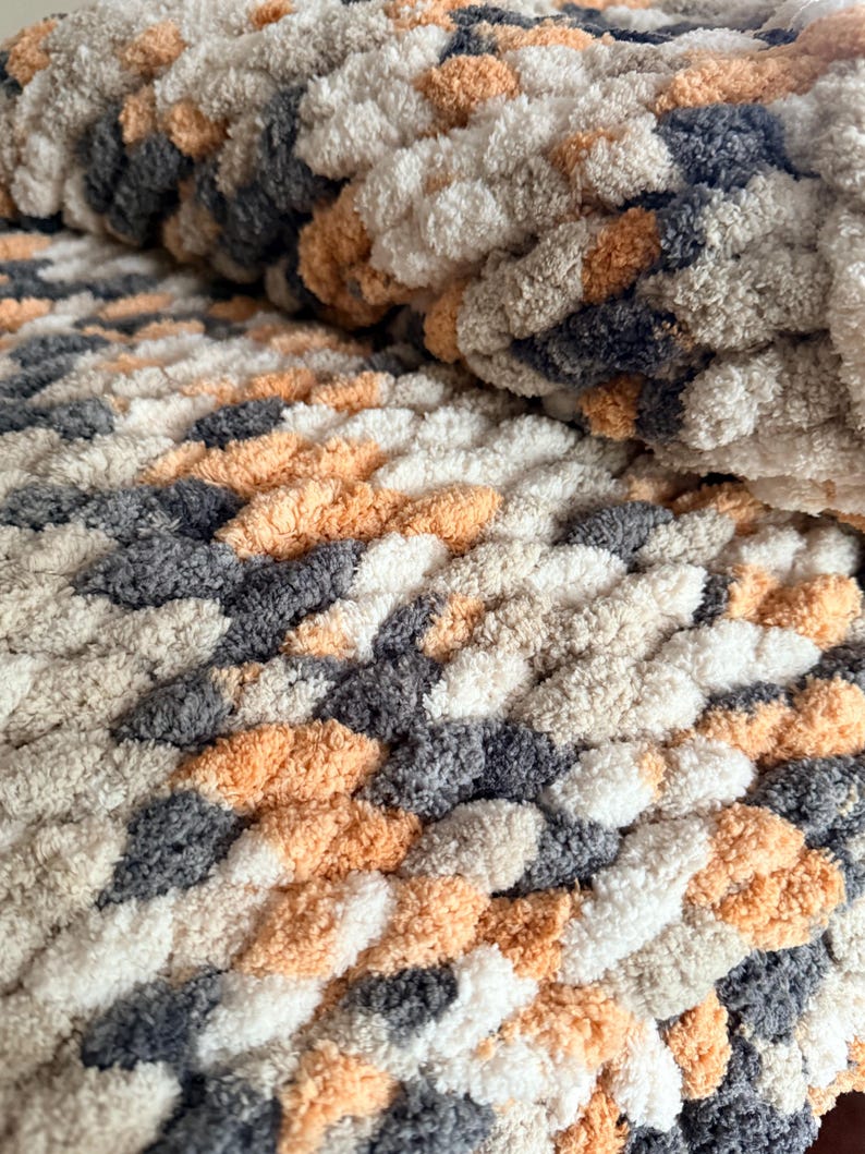 Close-up of chunky hand-knit blanket in Toasted Birch multi-tone yarn, showing plush stitches in cream, tan, and gray.
