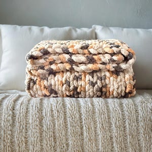 Hand-crafted chunky blanket in Toasted Birch colorway folded on cream bedspread for cozy neutral bedroom decor.