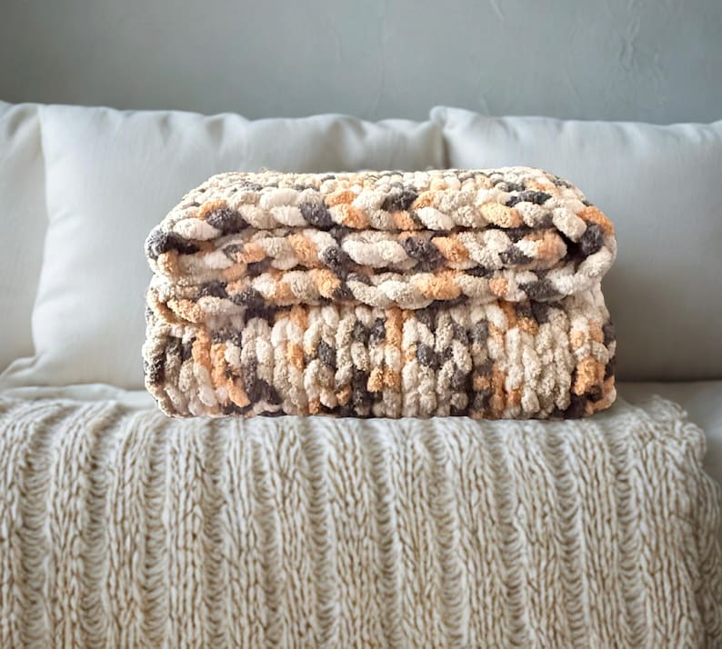 Hand-crafted chunky blanket in Toasted Birch colorway folded on cream bedspread for cozy neutral bedroom decor.