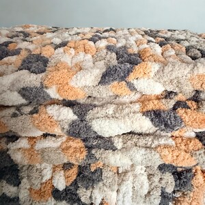 Close-up of Toasted Birch hand-knit blanket showing braided stitch detail and soft chenille yarn texture in gray, cream, and tan.