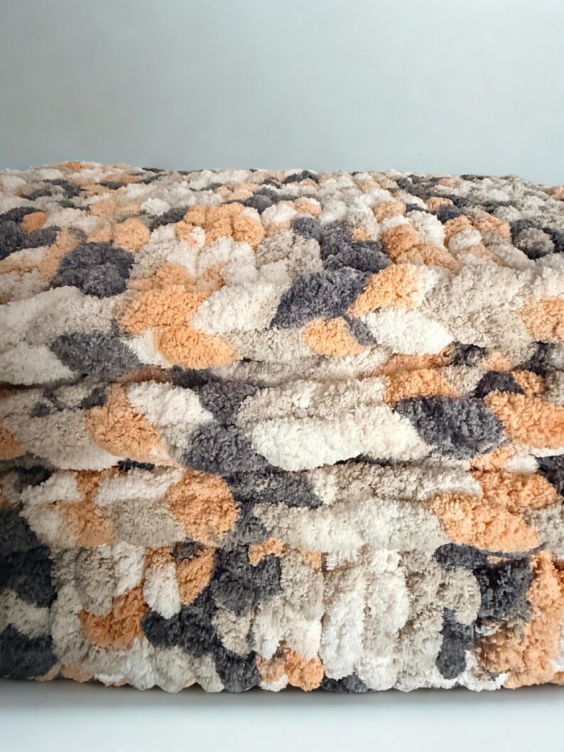 Close-up of Toasted Birch hand-knit blanket showing braided stitch detail and soft chenille yarn texture in gray, cream, and tan.