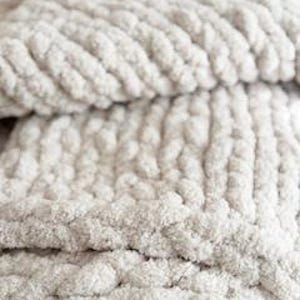 Close-up of French Vanilla chunky knit blanket showing thick braided stitches and plush chenille yarn texture in soft cream tone. The overall appearance suggests a cozy, warm, and comfortable home decor item, perfect for snuggling.