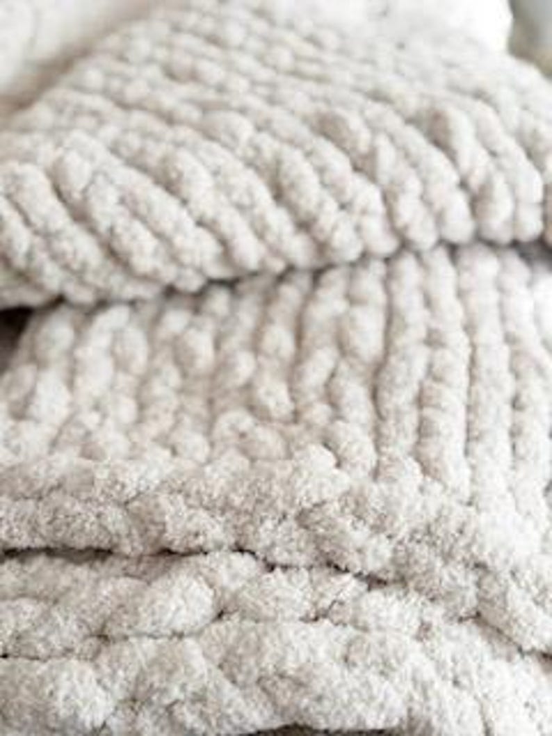 Close-up of French Vanilla chunky knit blanket showing thick braided stitches and plush chenille yarn texture in soft cream tone. The overall appearance suggests a cozy, warm, and comfortable home decor item, perfect for snuggling.