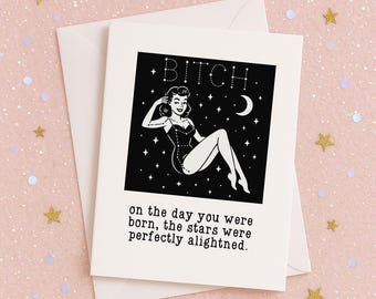 May include: A white greeting card with a black and white illustration of a woman in a swimsuit, the word "BITCH" above her, and the text "on the day you were born, the stars were perfectly alighted."