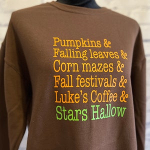May include: Brown sweatshirt with orange text that reads "Pumpkins & Falling leaves & Corn mazes & Fall festivals & Luke's Coffee & Stars Hallow"