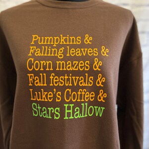 May include: Brown sweatshirt with orange text that reads "Pumpkins & Falling leaves & Corn mazes & Fall festivals & Luke's Coffee & Stars Hallow"