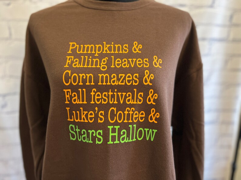 May include: Brown sweatshirt with orange text that reads "Pumpkins & Falling leaves & Corn mazes & Fall festivals & Luke's Coffee & Stars Hallow"