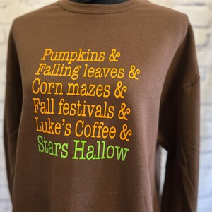May include: Brown sweatshirt with orange and green text that reads "Pumpkins & Falling leaves & Corn mazes & Fall festivals & Luke's Coffee & Stars Hallow"
