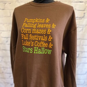 May include: Brown sweatshirt with the text "Pumpkins & Falling leaves & Corn mazes & Fall festivals & Luke's Coffee & Stars Hallow" in orange and green.