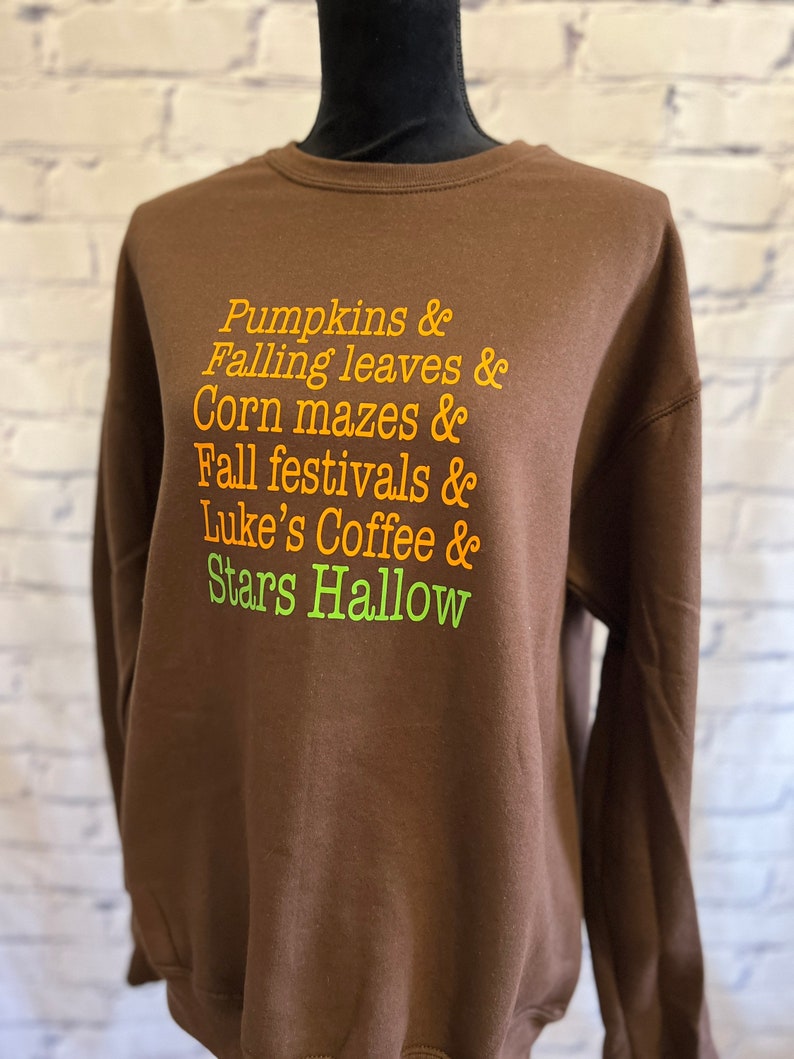 May include: Brown sweatshirt with the text "Pumpkins & Falling leaves & Corn mazes & Fall festivals & Luke's Coffee & Stars Hallow" in orange and green.