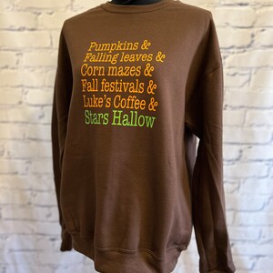 May include: Brown sweatshirt with the text "Pumpkins & Falling leaves & Corn mazes & Fall festivals & Luke's Coffee & Stars Hallow" printed in orange and green.
