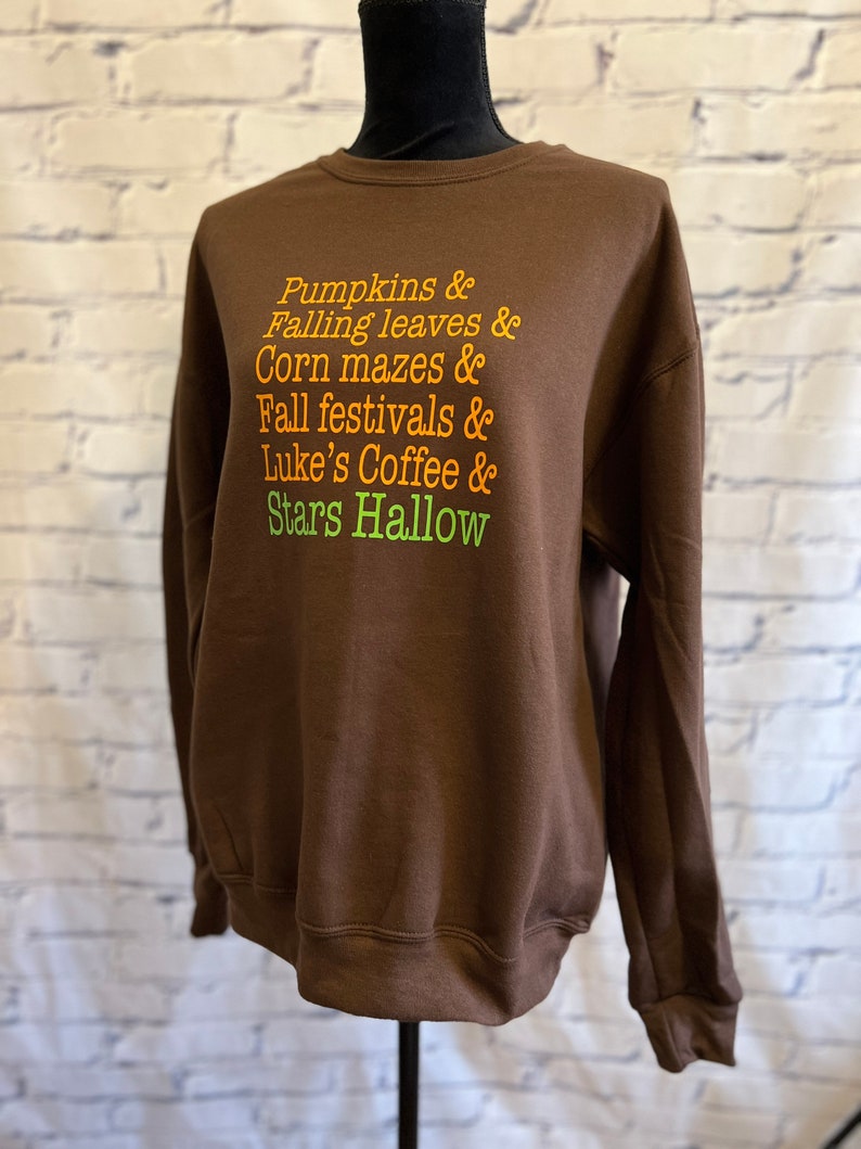 May include: Brown sweatshirt with the text "Pumpkins & Falling leaves & Corn mazes & Fall festivals & Luke's Coffee & Stars Hallow" printed in orange and green.