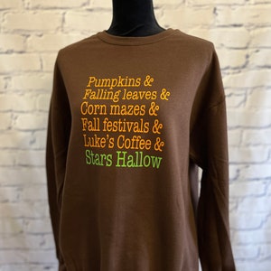 May include: Brown sweatshirt with the text "Pumpkins & Falling leaves & Corn mazes & Fall festivals & Luke's Coffee & Stars Hallow" printed in orange and green.