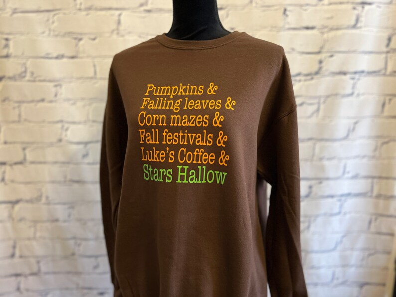 May include: Brown sweatshirt with the text "Pumpkins & Falling leaves & Corn mazes & Fall festivals & Luke's Coffee & Stars Hallow" printed in orange and green.
