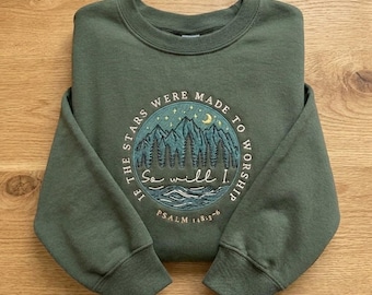 Puede incluir: Una sudadera verde oliva con un gráfico circular que presenta montañas, árboles, una luna creciente y el texto "If the stars were made to worship, so will I." También se incluye el texto "Psalm 148:3-6".