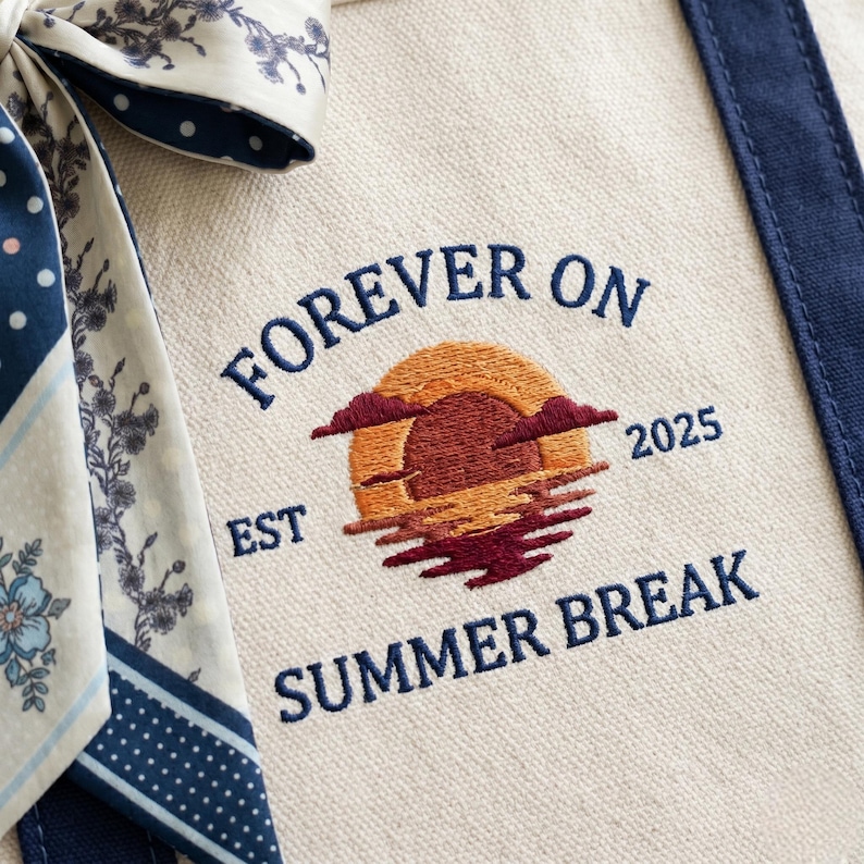 May include: A cream-colored canvas tote bag featuring dark blue embroidered text that reads FOREVER ON SUMMER BREAK with EST 2025. The center design shows an embroidered sunset in orange and maroon hues. A patterned fabric ribbon is tied to the side.