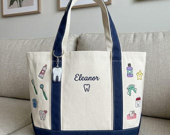 Puede incluir: Bolso tote de color crema con detalles y asas azul marino. Cuenta con pegatinas con temática dental y el nombre "Eleanor" con un gráfico de diente. Un llavero con forma de diente cuelga. Hecho de lona.