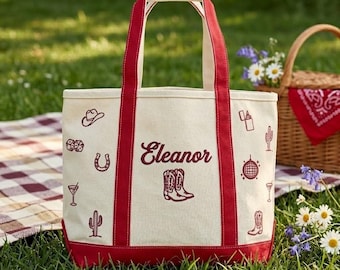 May include: A canvas tote bag with red accents and handles, personalized with the name "Eleanor". The bag features cowboy-themed illustrations and a red base, set against a grassy background.