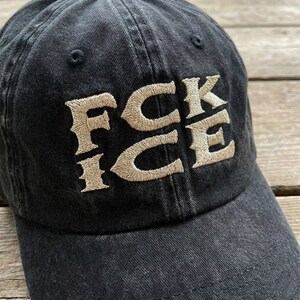 May include: Black baseball cap with the embroidered text "FCK ICE" in a tan color. The hat is made of a soft, worn fabric and has a curved brim. The hat is a casual accessory.