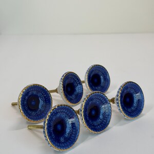 May include: A set of five round cabinet knobs featuring a deep blue center with a lighter blue patterned border and a gold-toned rim. Each knob has a metallic threaded bolt extending from the back for installation on furniture or cabinetry.