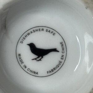Może przedstawiać: Biały ceramiczny talerz z czarną sylwetką ptaka wewnątrz okrągłej obw&oacute;dki. Obw&oacute;dka zawiera tekst "Dishwasher Safe", "Made in China" i "Fabriqu&eacute; en Chine".