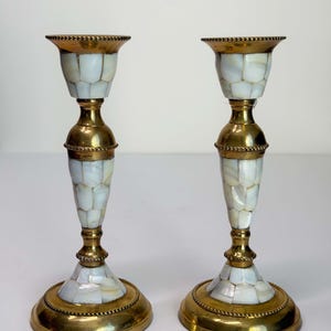 May include: A pair of matching candlestick holders featuring a polished brass frame with a decorative beaded edge. The central column and base are inlaid with small, iridescent white mother-of-pearl tiles arranged in a mosaic pattern.