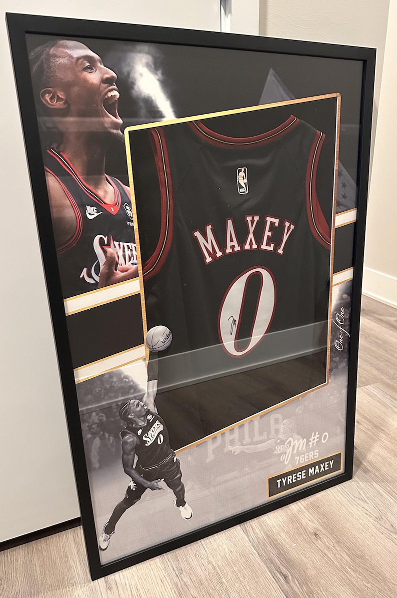 May include: Framed basketball jersey of Tyrese Maxey, number 0, in black with red trim. The frame includes images of the player in action and the text "PHILADELPHIA 76ERS". The jersey is signed.