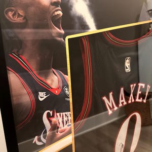 May include: Framed basketball jersey featuring the name "MAXEY" and the number "0" in white. The jersey is black with red and white accents. The image also includes a portrait of a basketball player wearing the jersey.