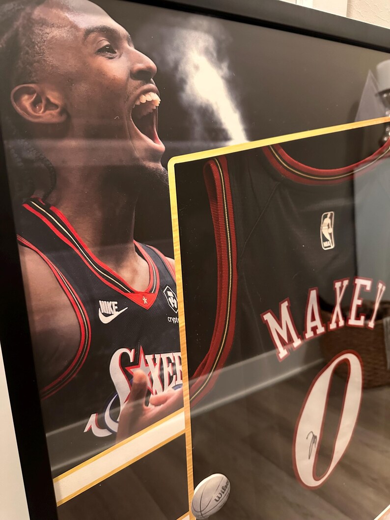 May include: Framed basketball jersey featuring the name "MAXEY" and the number "0" in white. The jersey is black with red and white accents. The image also includes a portrait of a basketball player wearing the jersey.