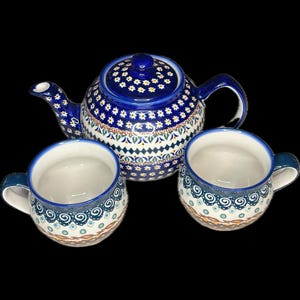 May include: A blue and white ceramic tea set with a teapot and two mugs. The teapot and mugs have a floral pattern with blue accents. The set is designed for serving tea. The teapot measures approximately 20 cm in height.