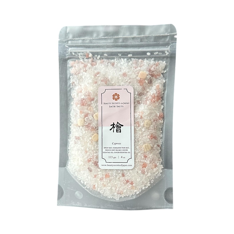 May include: A clear resealable pouch filled with white and pink bath salts mixed with small wooden cubes. The label reads Beauty Secrets of Japan Bath Salts, Cypress, with ingredients including Epsom salt, Himalayan pink salt, and 113 grams or 4 ounces.