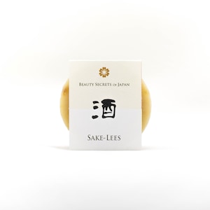 May include: A circular, pale-yellow product with a white label. The label displays the text "BEAUTY SECRETS OF JAPAN", Japanese characters, and "SAKE-LEES" in black. The background is plain white.