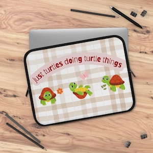 Può includere: Custodia per laptop con cerniera nera e motivo a quadri beige e bianco. La custodia presenta il testo "just turtles doing turtle things" e illustrazioni di tartarughe dei cartoni animati, un fiore e una farfalla.