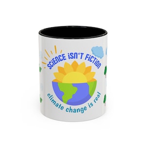 May include: White ceramic mug with a black interior, featuring a design of a sun over a split earth, with the text "SCIENCE ISN'T FICTION" and "climate change is real" in blue. The mug has green trees and clouds around the sides.