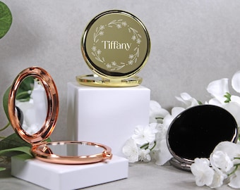 Peut inclure: Trois miroirs compacts : or, or rose et noir. Le miroir doré porte le nom "Tiffany" entouré d'un motif floral. Le miroir or rose est ovale, et le miroir noir est rond. Ils sont présentés sur des socles blancs.